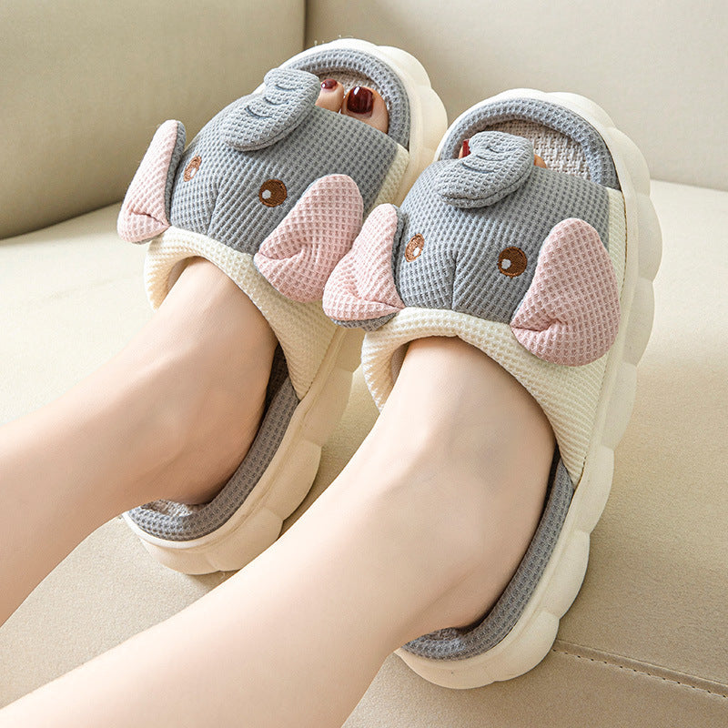 Pair of cartoon elephant slippers worn by a person on a beige couch.