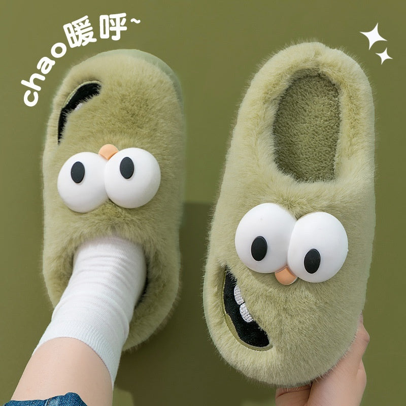 Green slippers with cartoon face design held by a person against a green background